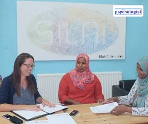 Two Somali women with headscarves smile towards the author. They are sat at a table covered in papers.