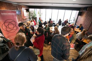 A large group is scattered around a room in the Watershed.