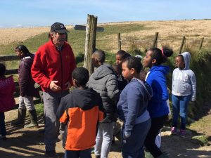 A group of children in listening to an older man. They are stood by a signpost.