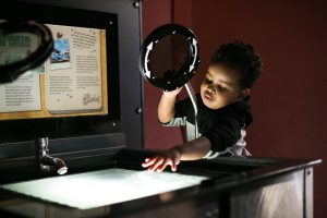 A little boy reaches for a square of light while moving a magnifying glass