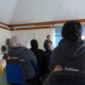 Two women in Autism Independence sweatshirts watch Aga give her presentation