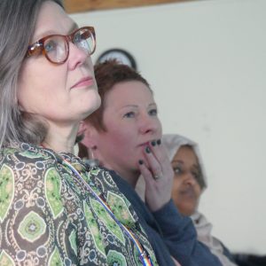 Rosi, Aga and Nura sit in a row, watching Shane talk about the project