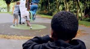 A young boy is watching another group of children playing.